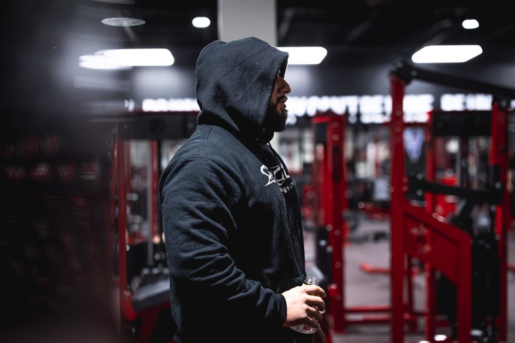 Side view of a man in a hoodie holding a bottle in a modern gym setting.